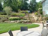 Hillside and natural stone walls above a patio and lawn area, beautifully landscaped with an assortment of plant life.